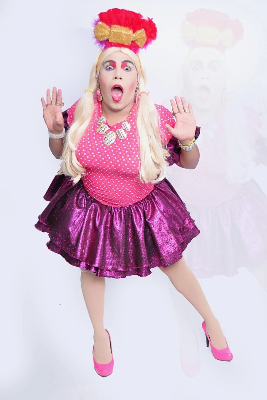 Junior Paiva como Damiana Star, de peruca loira e saia rosa brilhante, fazendo cara de espanto